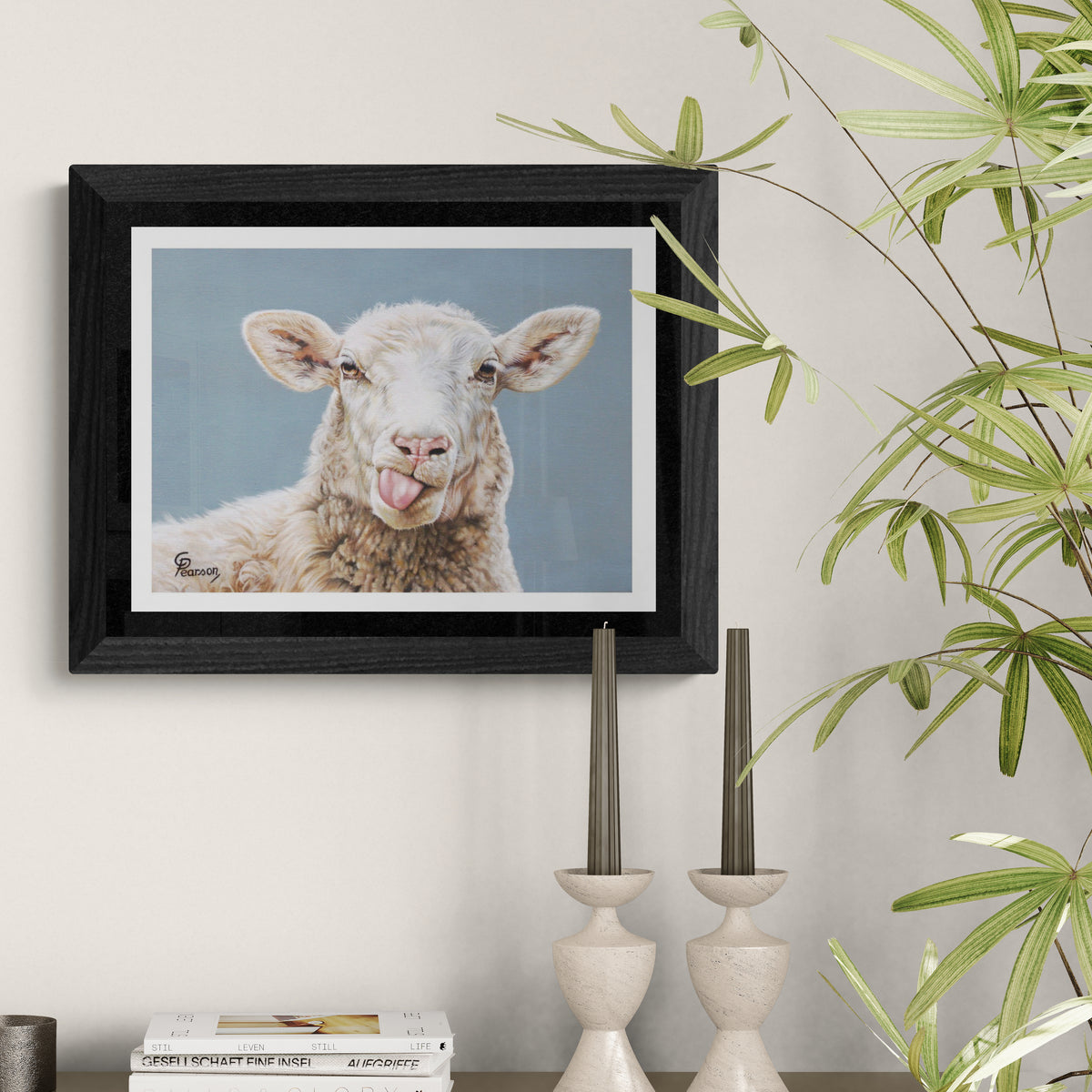 Framed picture of a lamb with a tongue sticking out on a wall with plants and decor.
