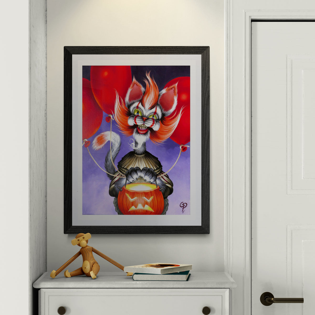 Framed artwork of a colorful haloween cat  clown with red balloons on a white wall.
